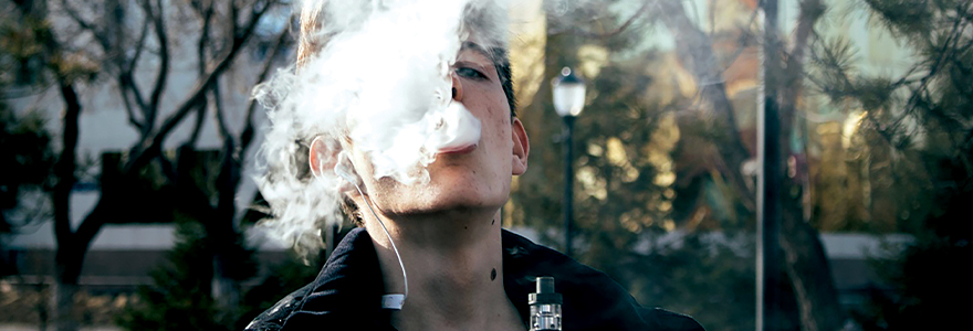 Image of a teenager vaping and blowing smoke into the air